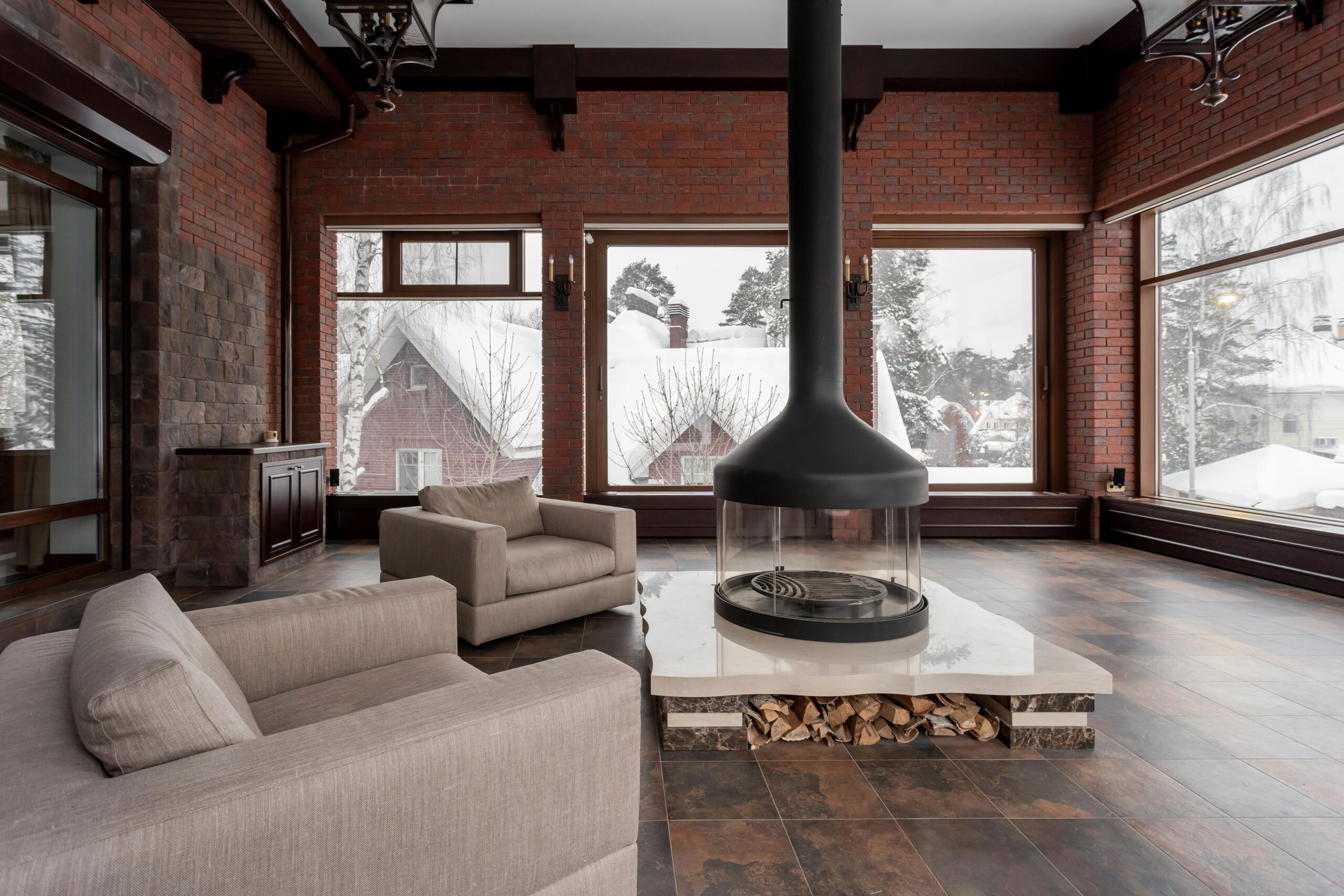 A luxury modern living room renovation in Cumbria featuring professional exposed brickwork, large panoramic windows, and a central designer fireplace.